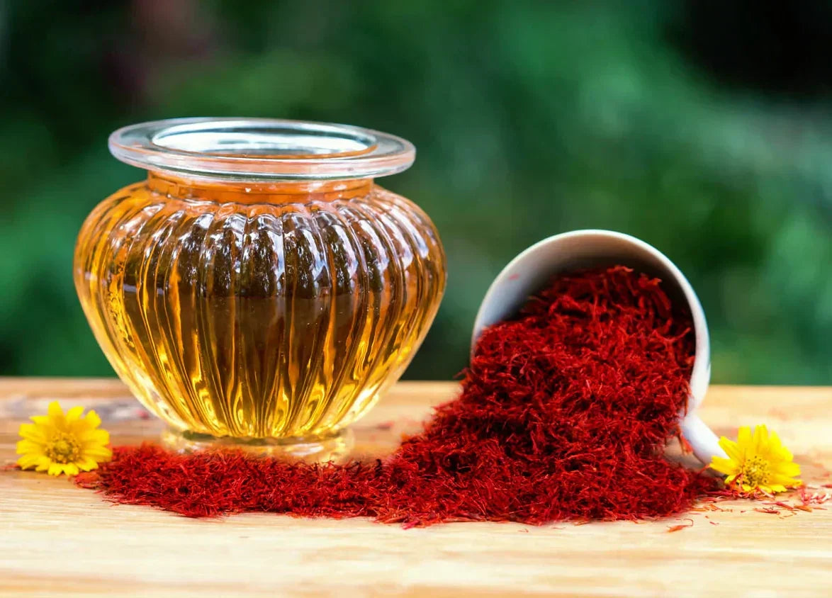 Glass jar of golden saffron infusion beside a bowl of saffron threads
